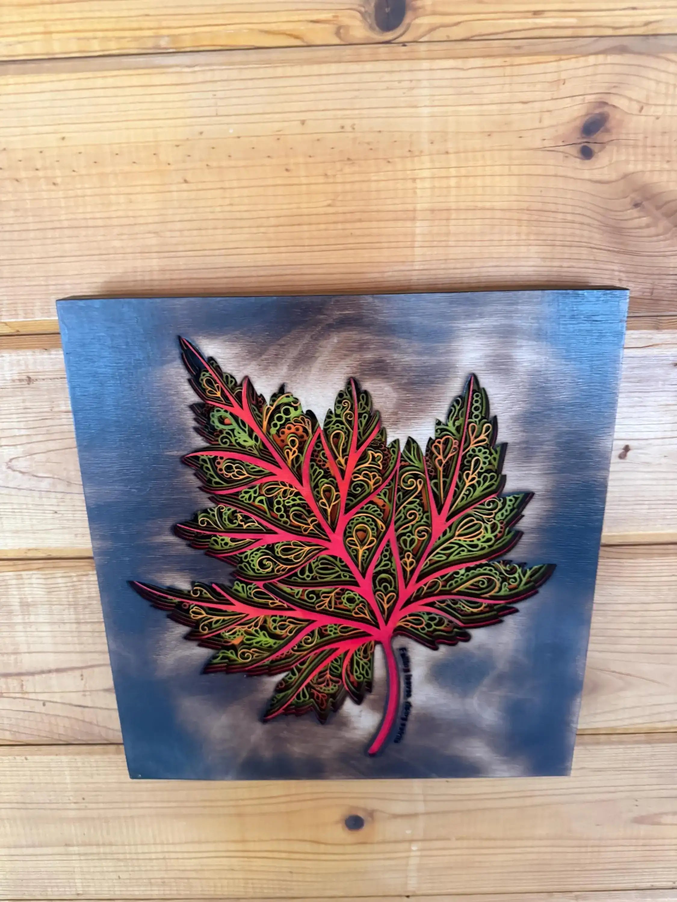 Layered wood art maple leaf with intricate mandala patterns on blue background