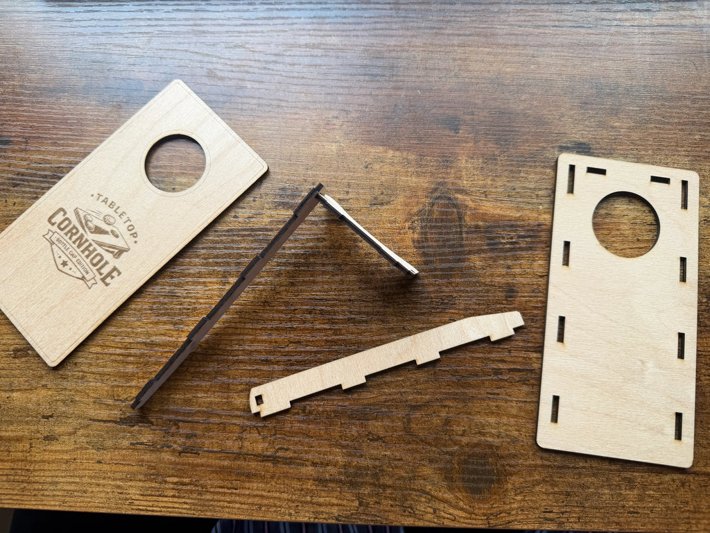 Handcrafted wooden tabletop cornhole game set with laser-cut pieces on rustic wood surface