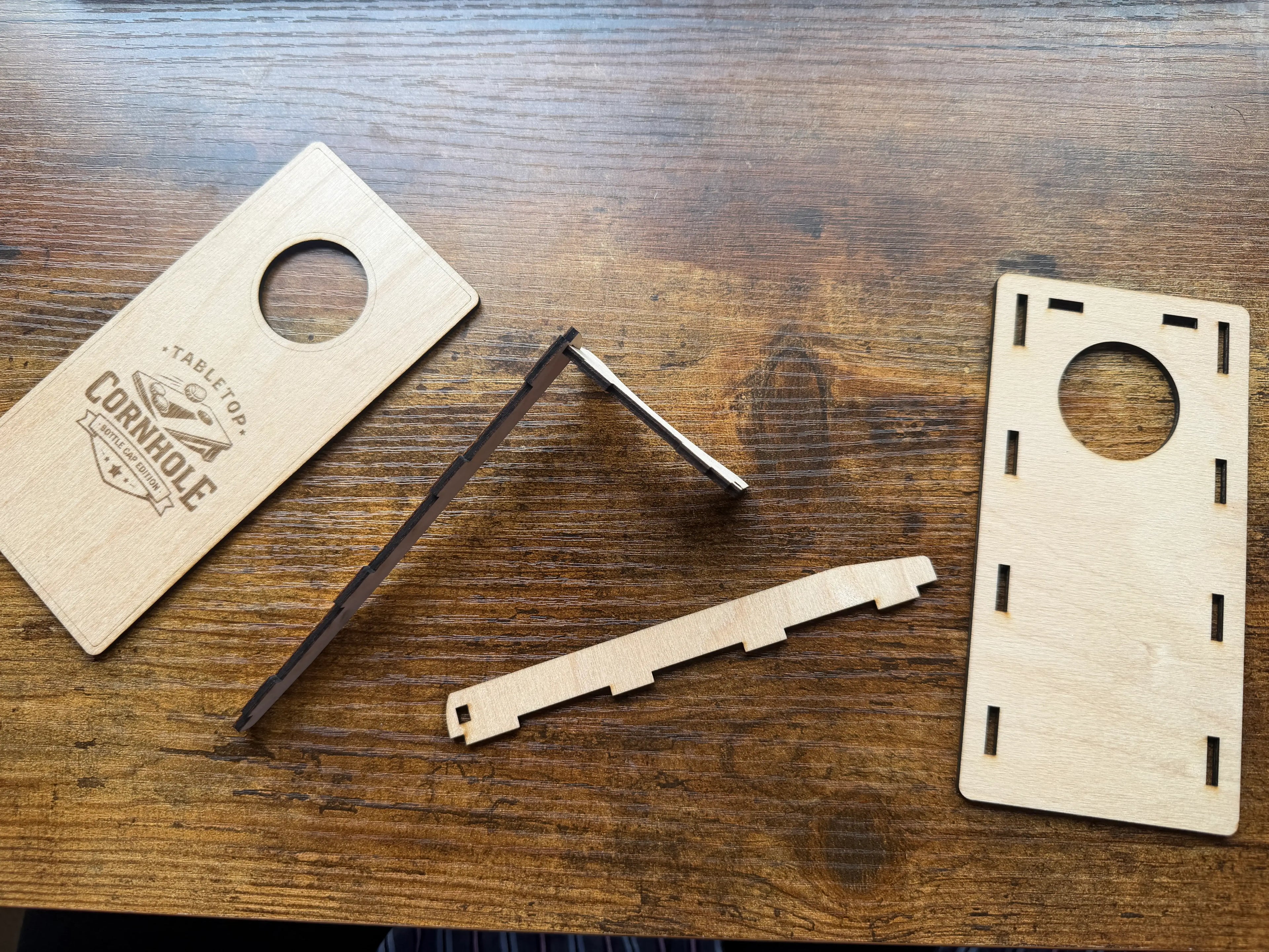 Handcrafted wooden tabletop cornhole game set with laser-cut pieces on rustic wood surface