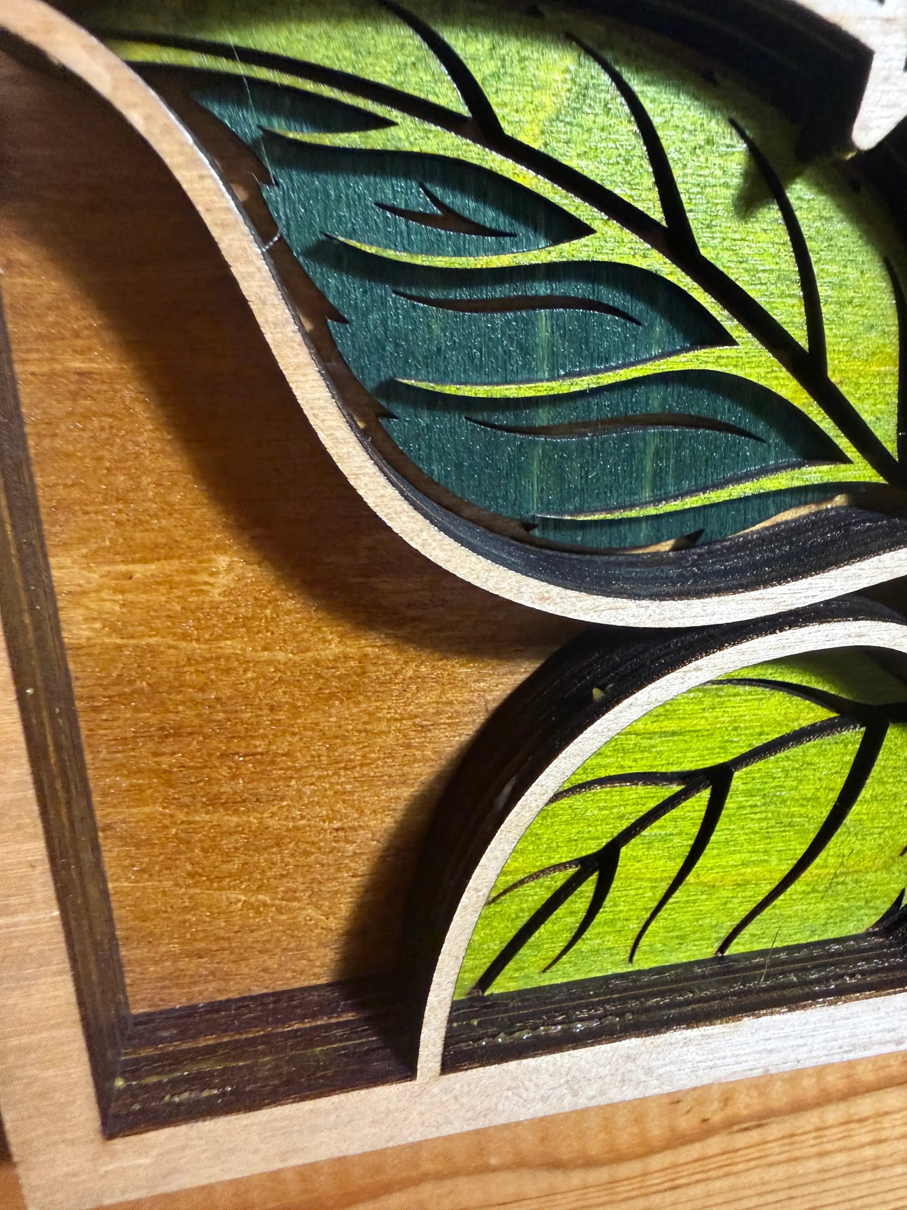 Layered wood art with laser-cut leaf design, green and teal tones, natural wood frame