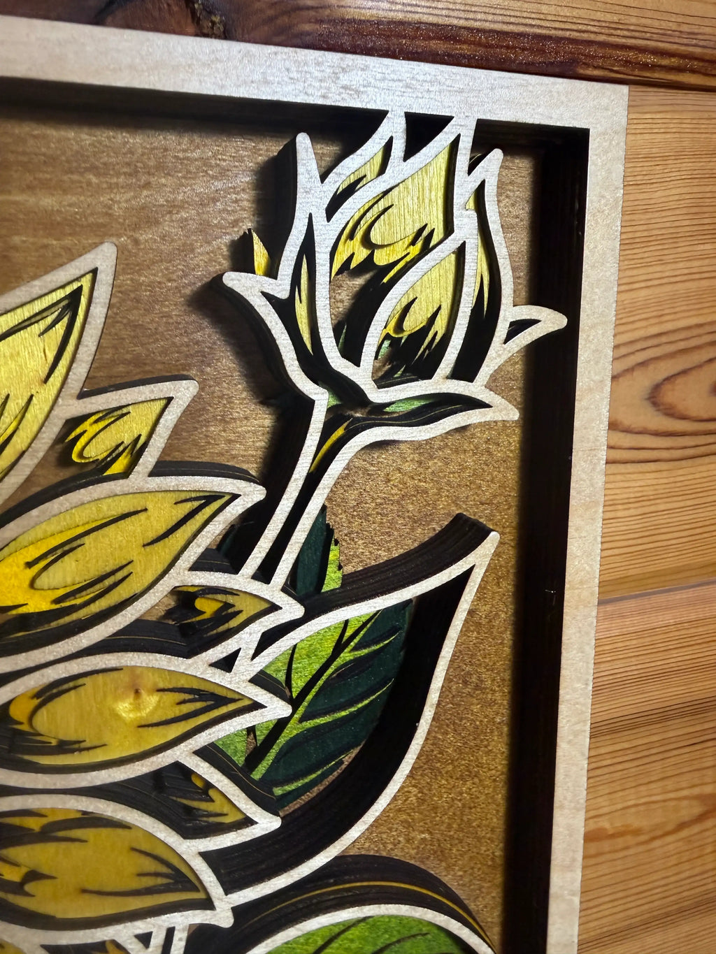 Layered wood art featuring sunflower design with yellow petals and green leaves, handcrafted decor