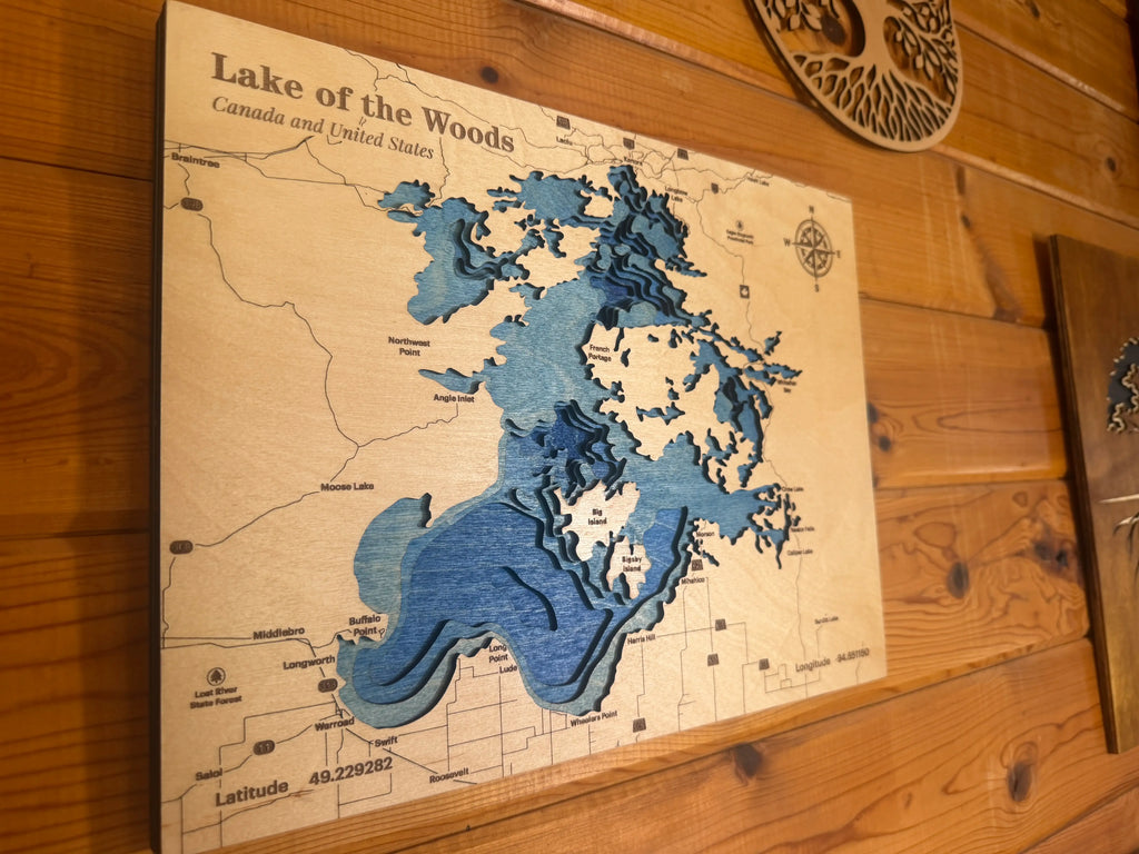 Layered wood art map of Lake of the Woods, Canada and US, with blue depth layers and compass rose.