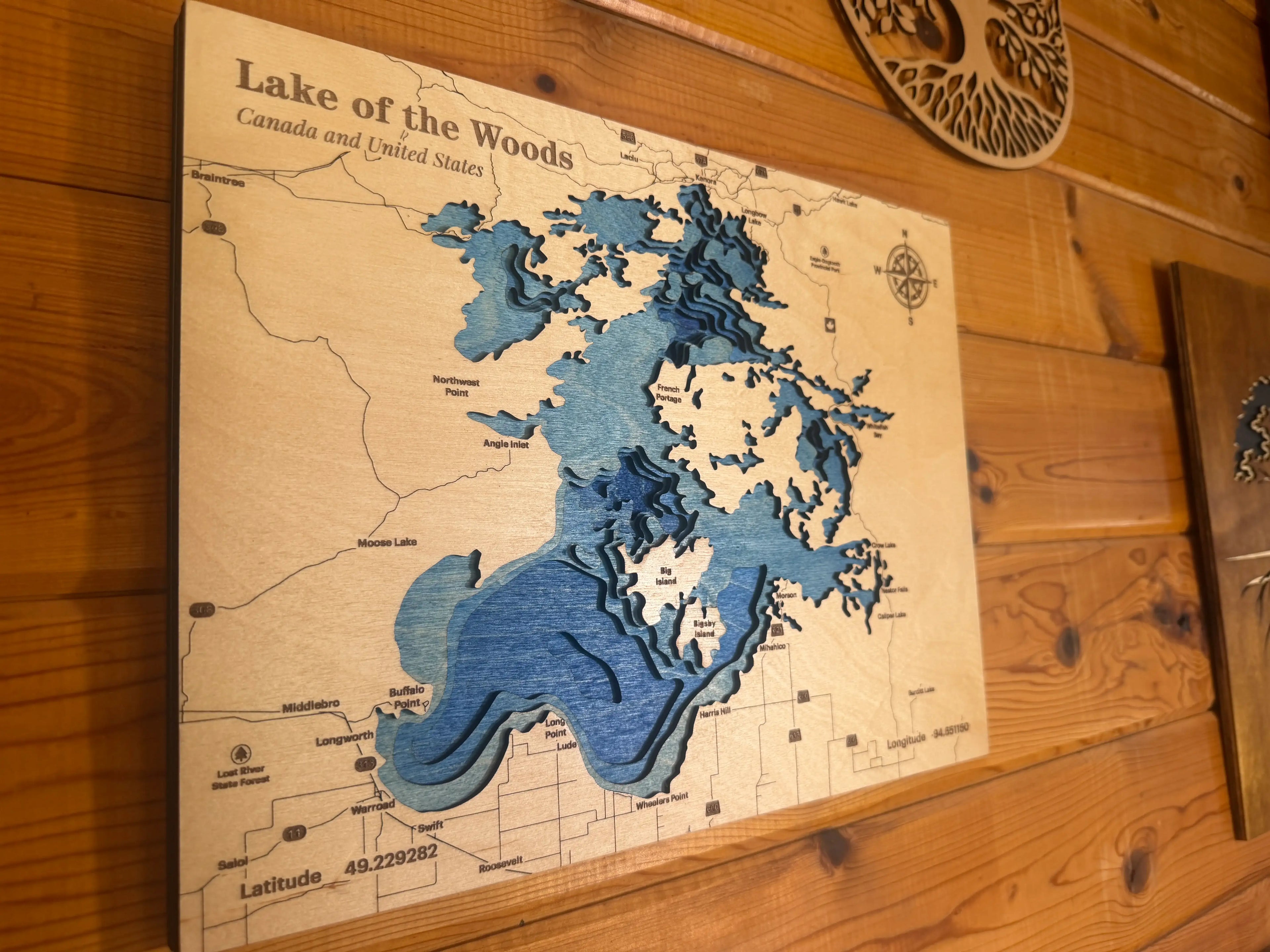 Layered wood art map of Lake of the Woods, Canada and US, with blue depth layers and compass rose.
