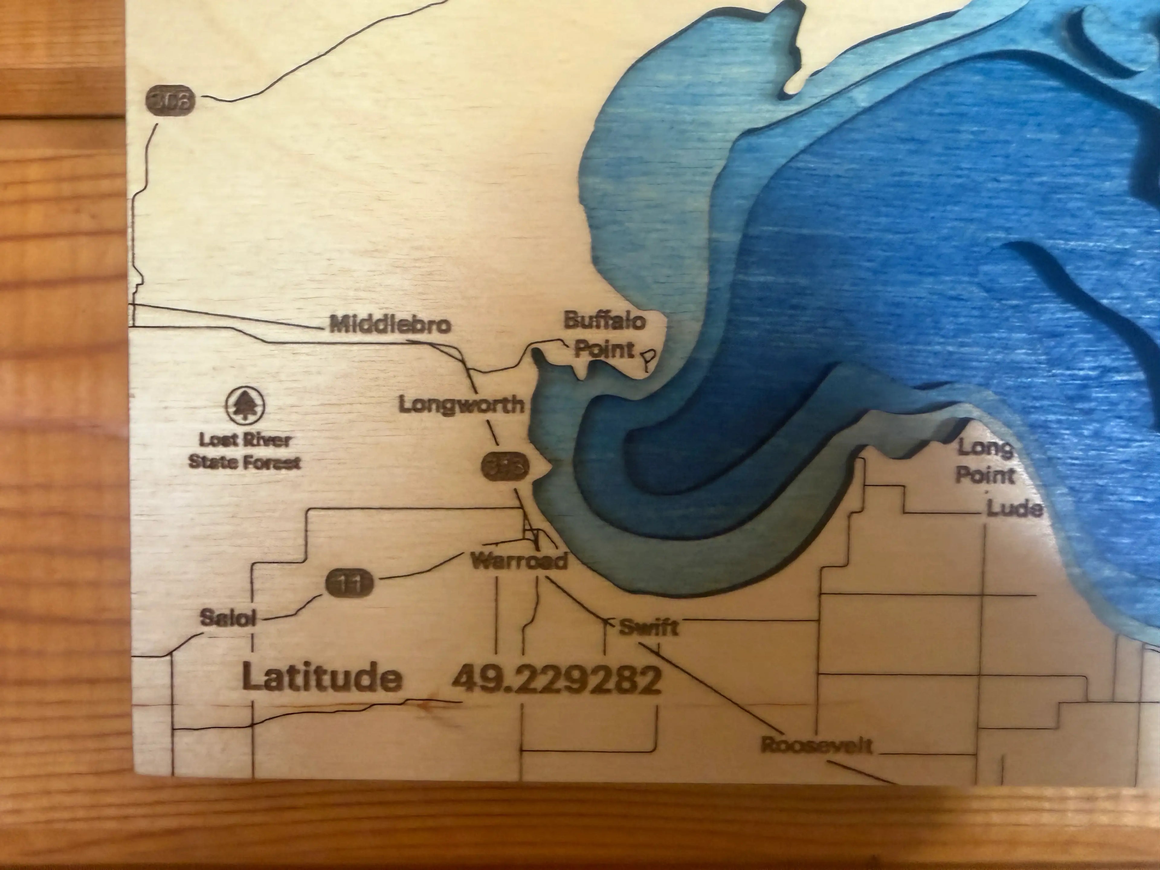 Layered wood lake map with blue depth layers, labeled towns, and latitude detail