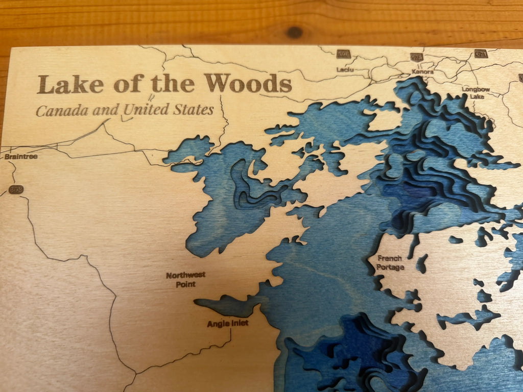 Layered wood art map of Lake of the Woods, Canada and United States, featuring blue depth layers and labeled points.
