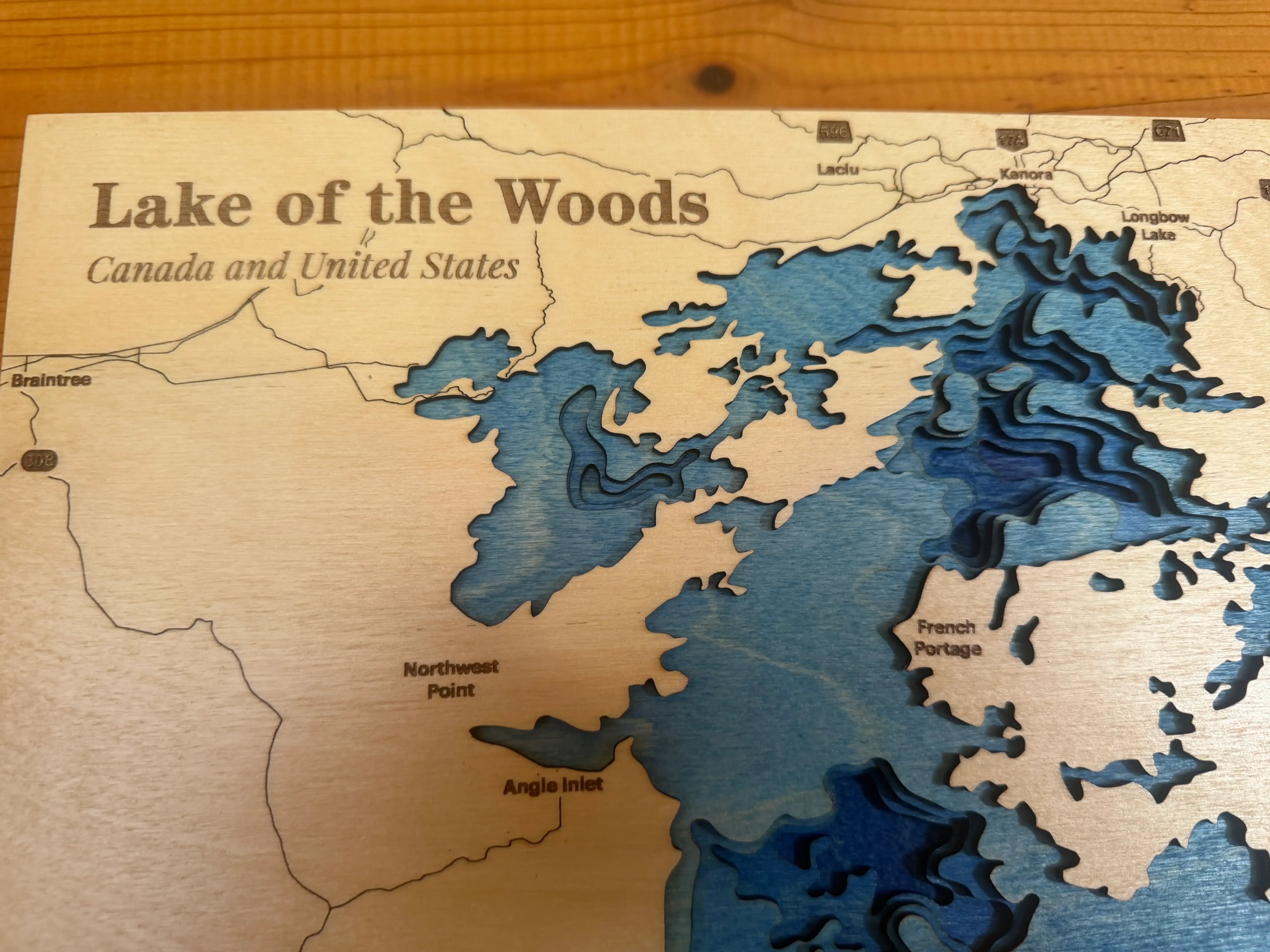 Layered wood art map of Lake of the Woods, Canada and United States, featuring blue depth layers and labeled points.