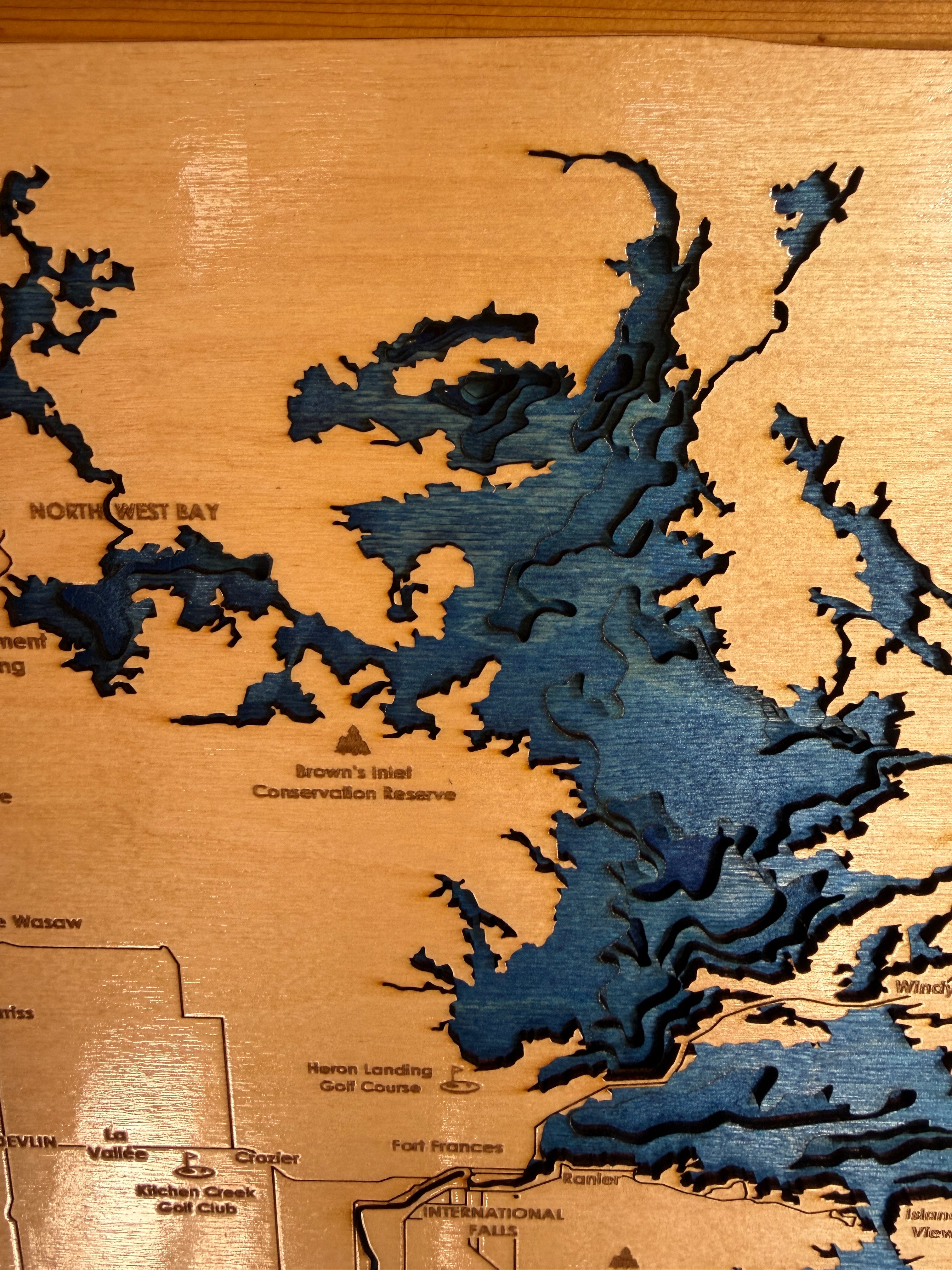 Wooden map with laser-cut topography, showing water bodies and land features.