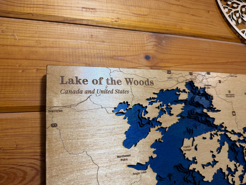 Handcrafted layered wood map of Lake of the Woods, Canada and USA, featuring blue water depth layers and engraved locations.