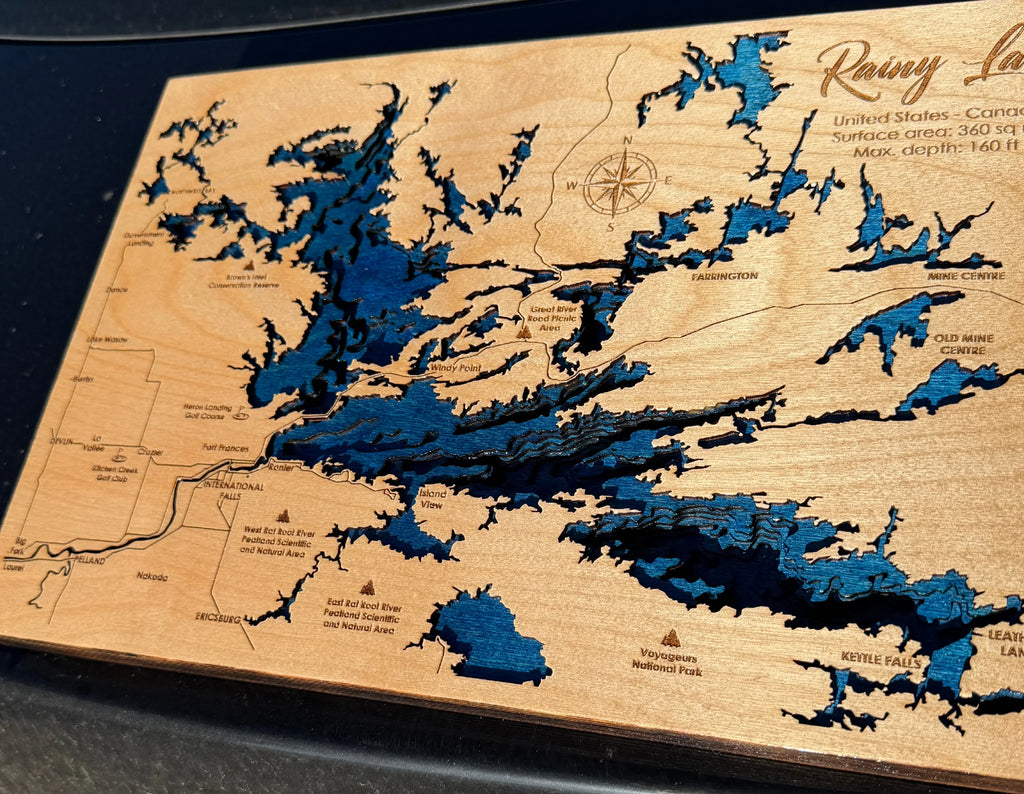 Layered wood map of Rainy Lake with blue water depths, laser-cut details, and engraved landmarks for rustic home decor.