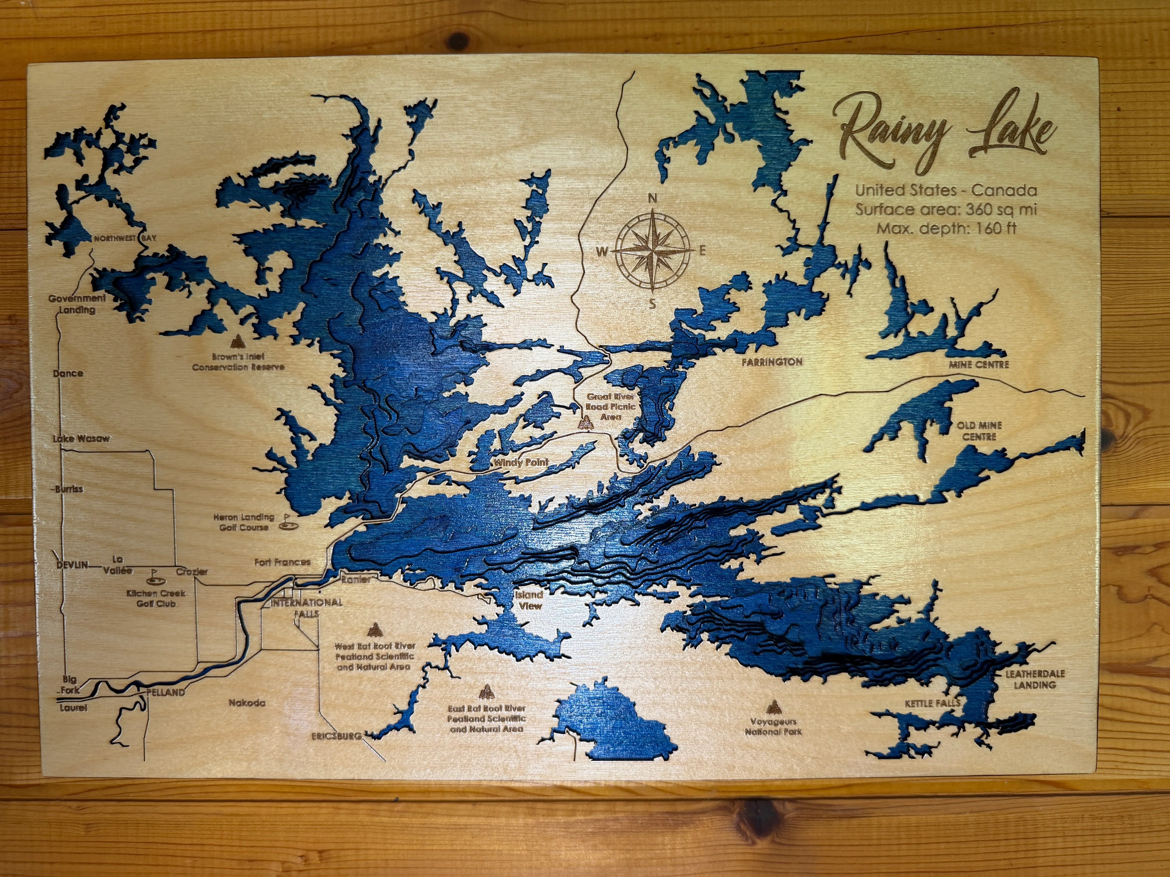 Handcrafted wooden map of Rainy Lake, USA-Canada border, featuring layered blue depth contours and engraved landmarks for rustic wall decor.
