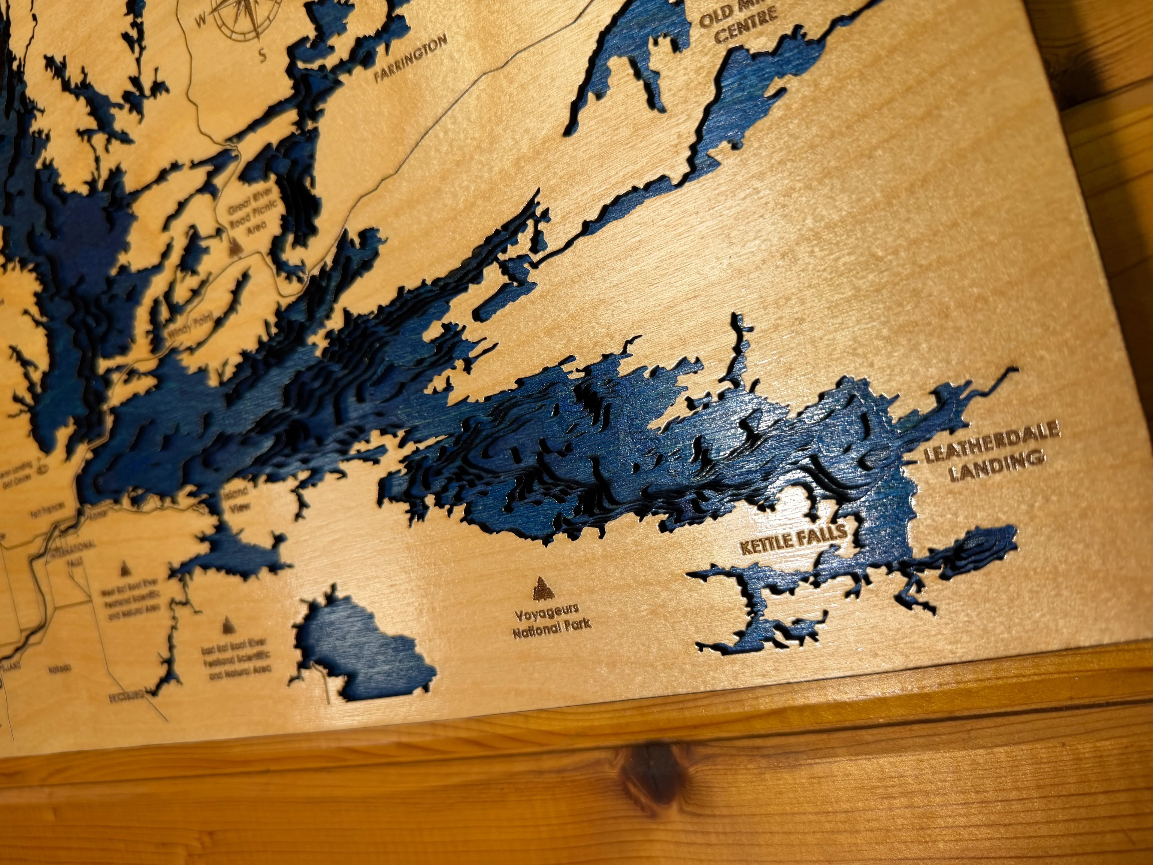 Layered wood lake map with blue water depths, showing Kettle Falls and Voyageurs National Park, handcrafted decor.