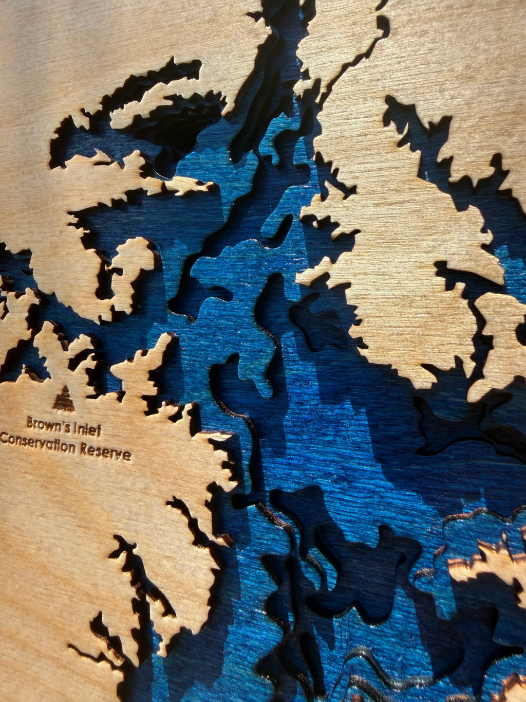Layered wood lake map art with blue water and engraved Brown's Inlet Conservation Reserve text, handcrafted decor.