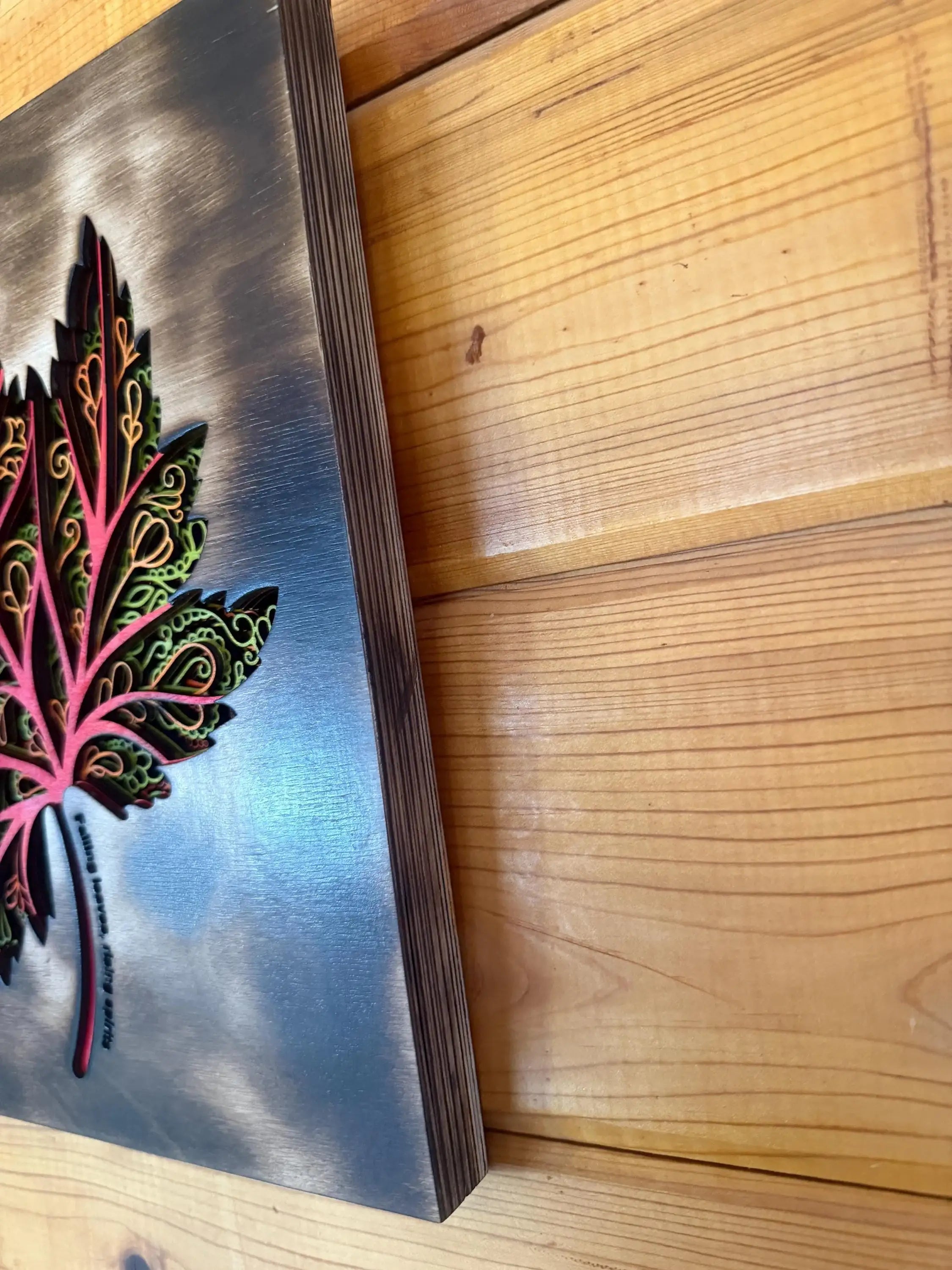 Layered wood art featuring a vibrant, intricately designed maple leaf on a metallic background.