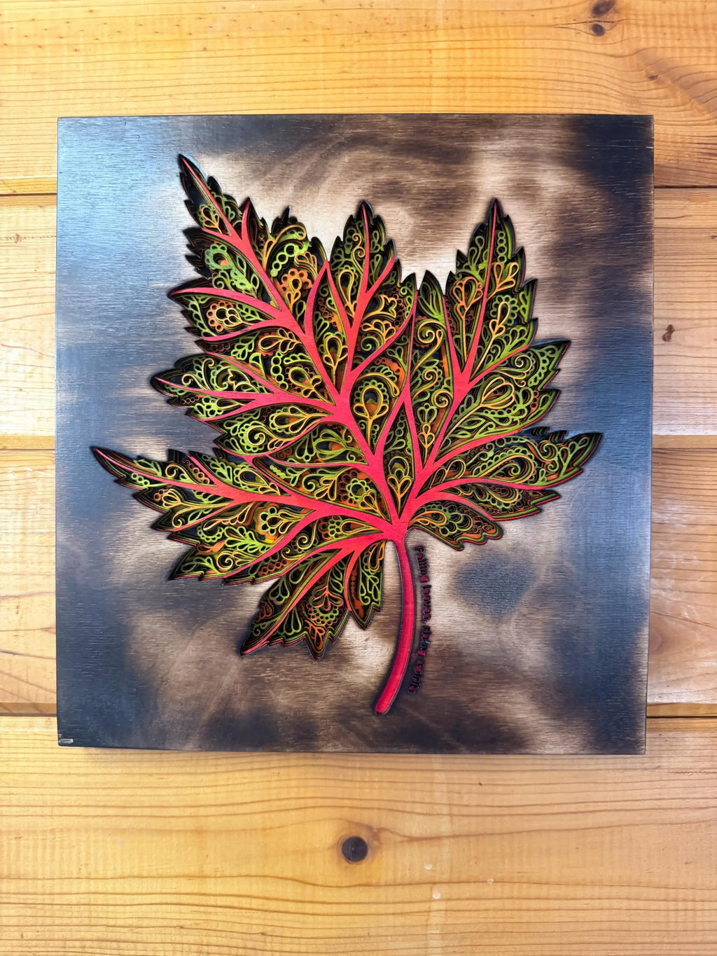 Layered wood art maple leaf with intricate patterns, vibrant red and green hues, handcrafted decor