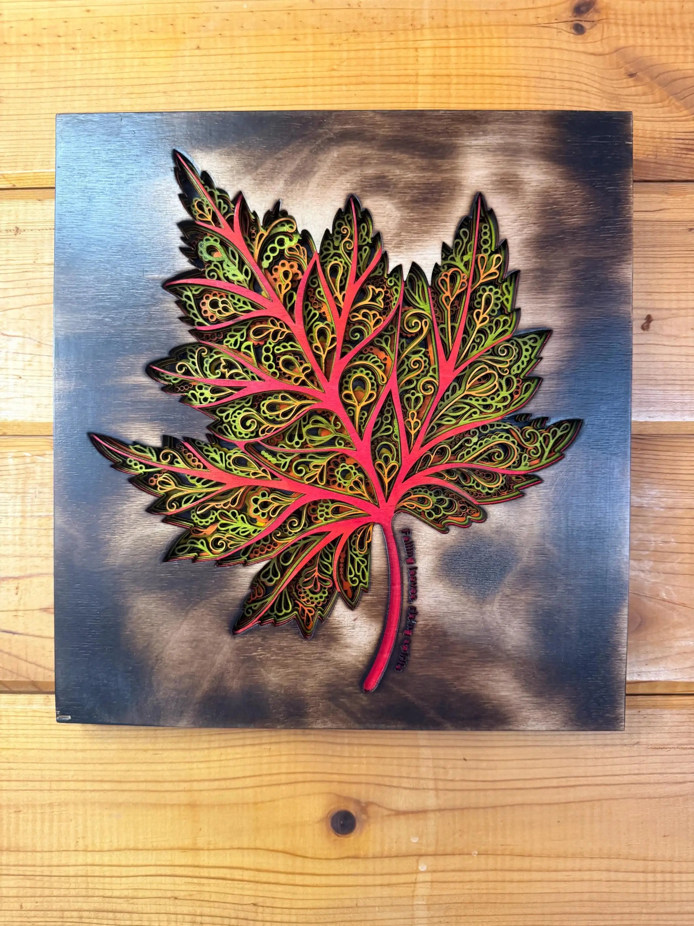 Layered wood art maple leaf with intricate patterns, vibrant red and green hues, handcrafted decor