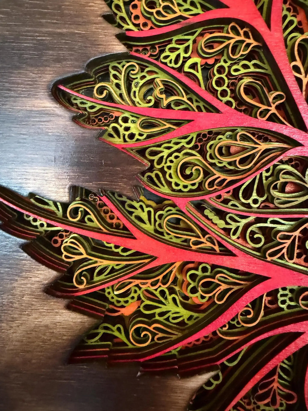 Layered wood art with intricate mandala patterns in vibrant red, green, and gold tones.