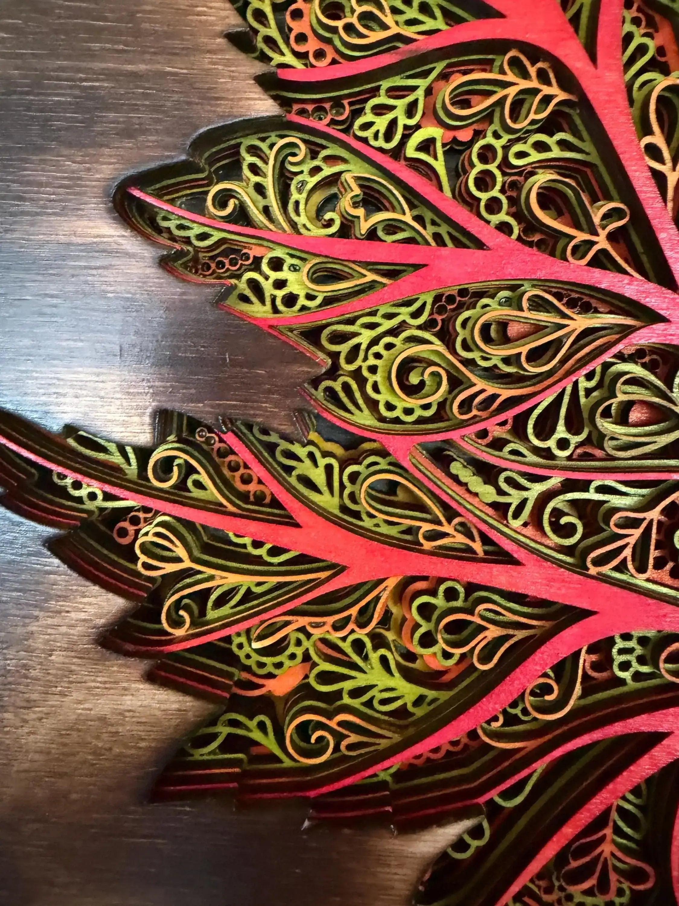 Layered wood art with intricate mandala patterns in vibrant red, green, and gold tones.