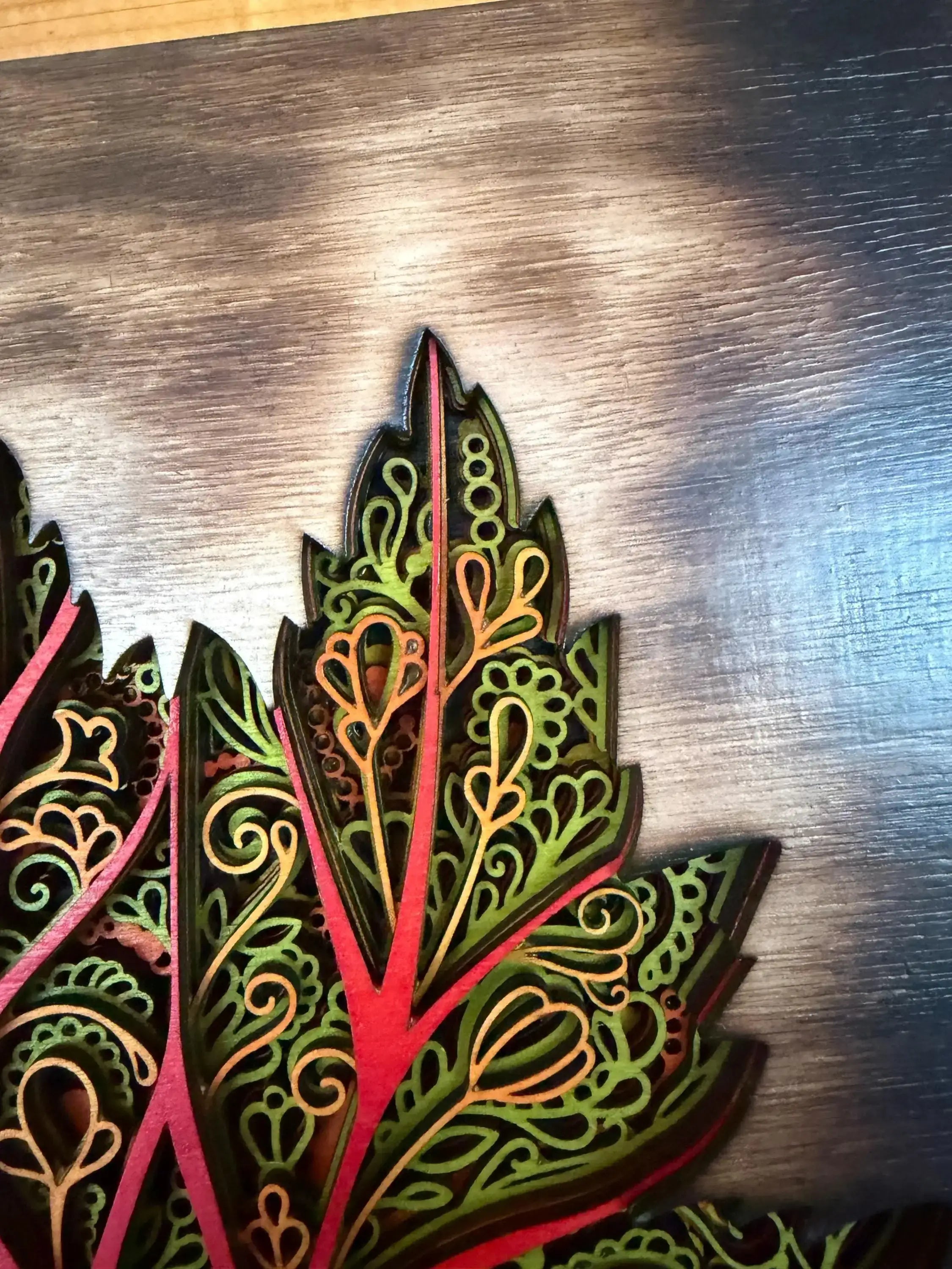 Intricate layered wood art with vibrant green and red leaf designs, handcrafted for unique home decor.
