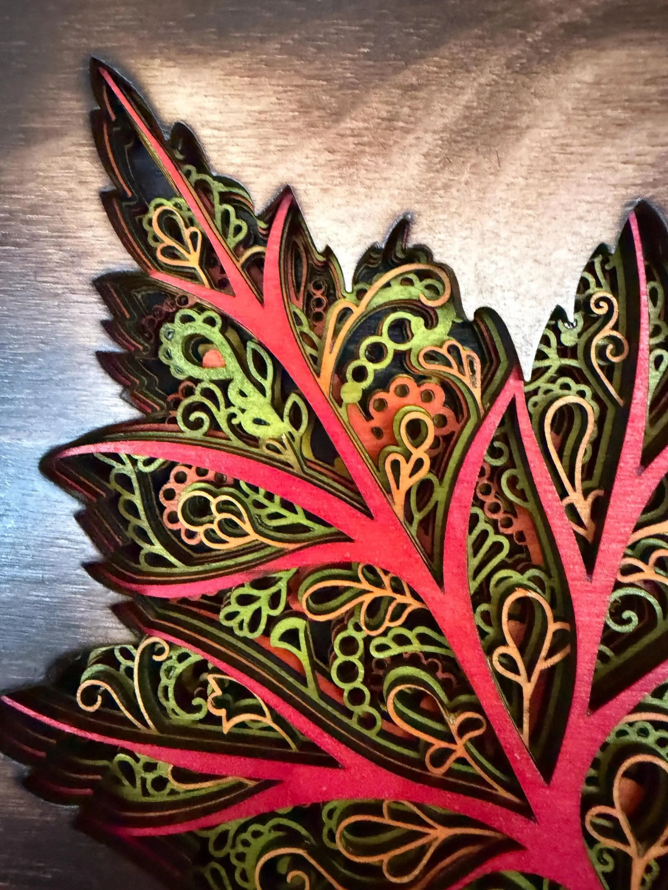 Layered wood mandala art with intricate red, green, and gold laser-cut patterns on rustic wood background