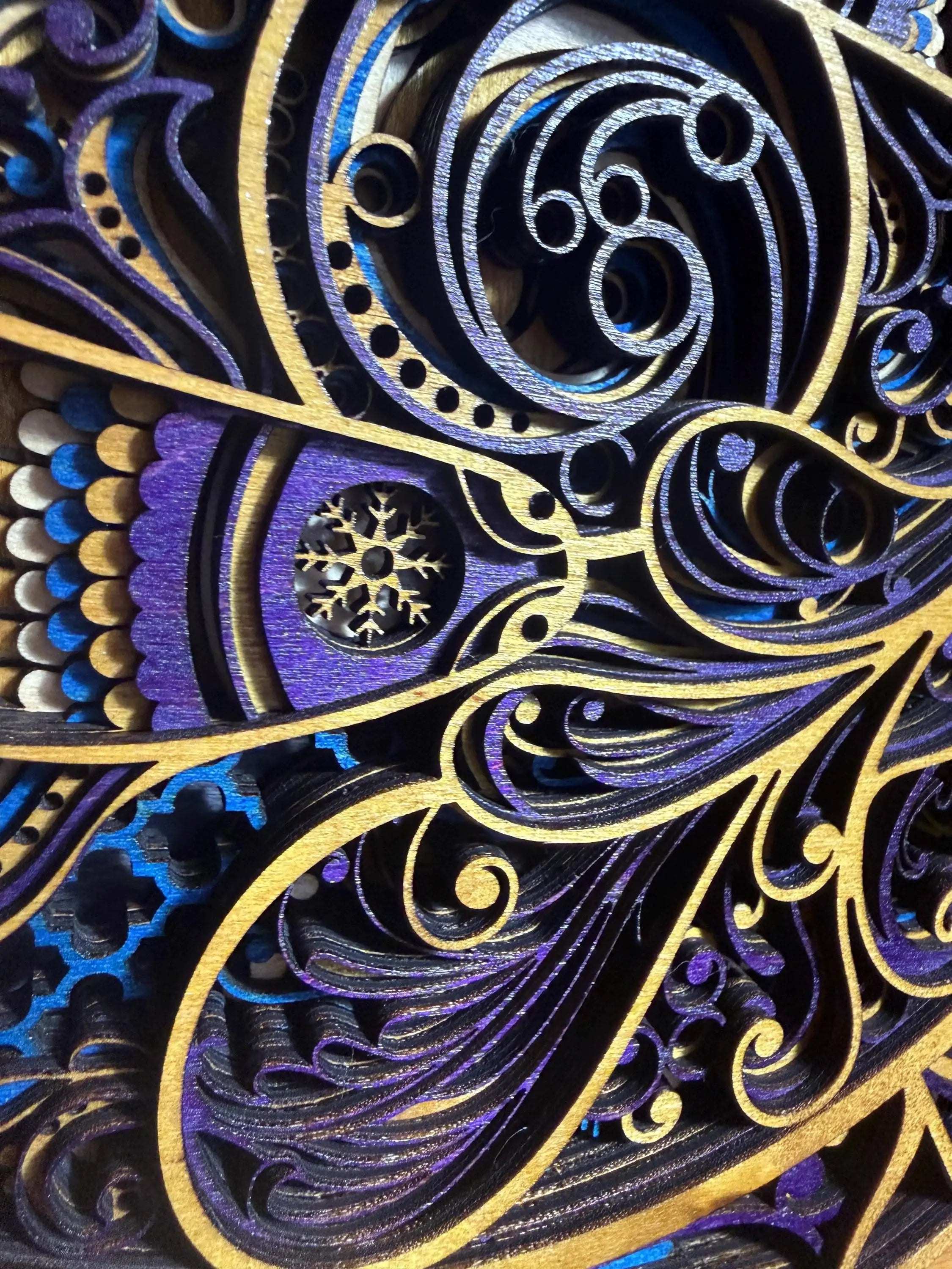 Intricate layered wood art with purple, blue, and gold swirls, featuring a snowflake cutout and detailed laser-cut patterns.