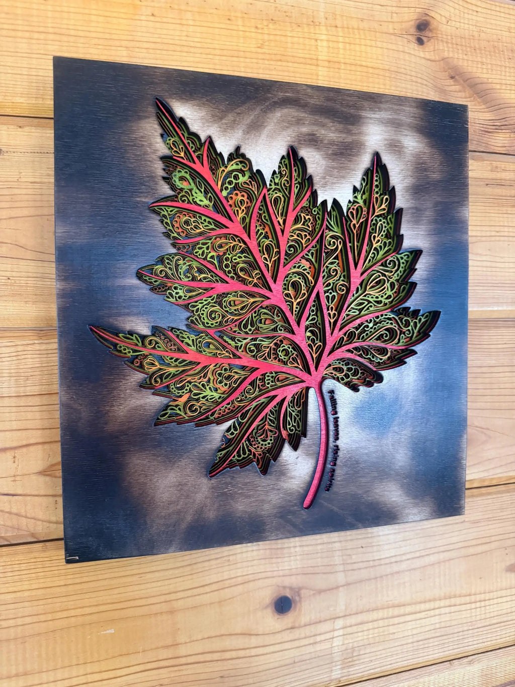 Intricate layered wood maple leaf art with pink veins, green filigree, and blue-gray background, handcrafted decor