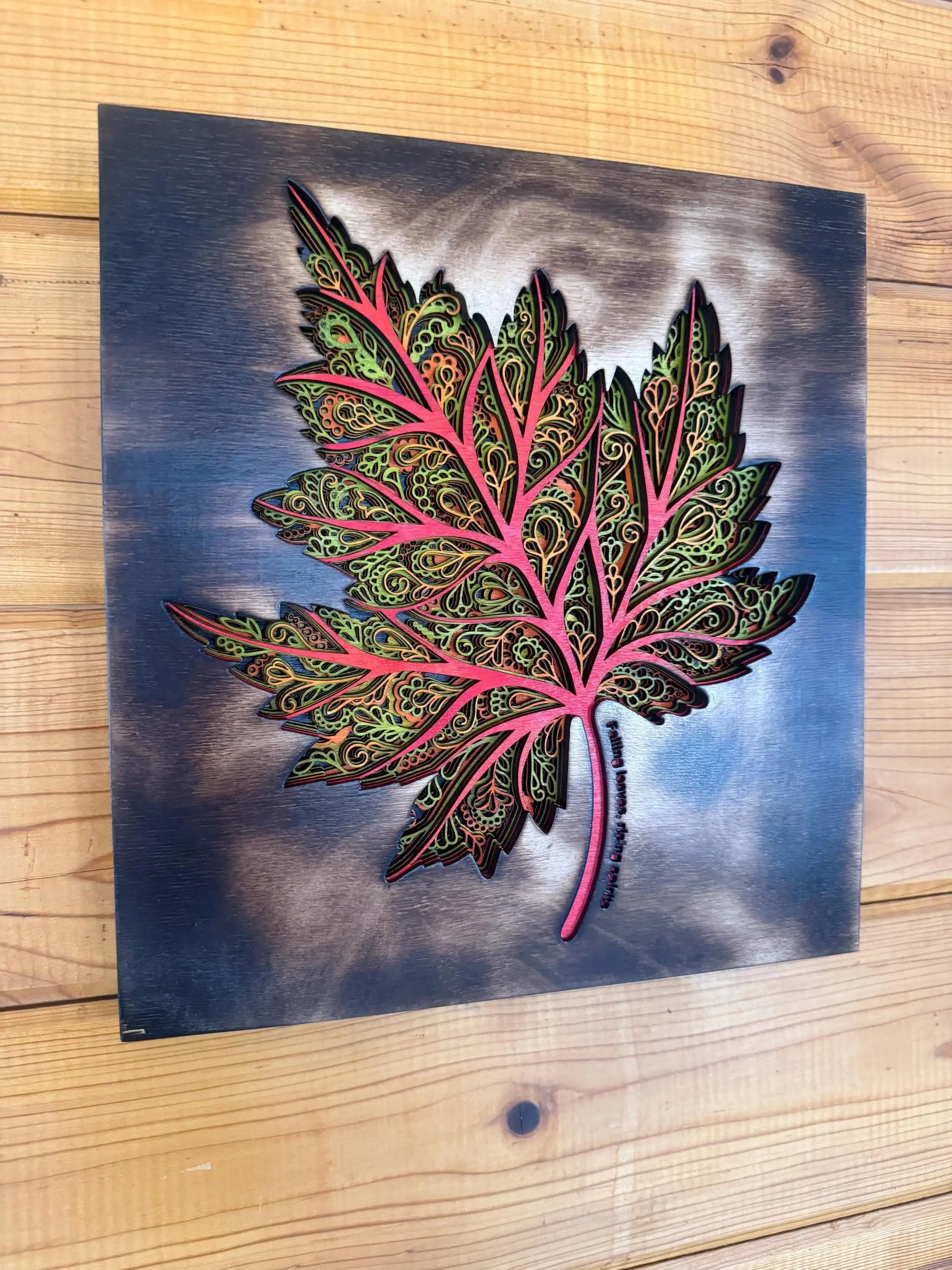 Intricate layered wood maple leaf art with pink veins, green filigree, and blue-gray background, handcrafted decor