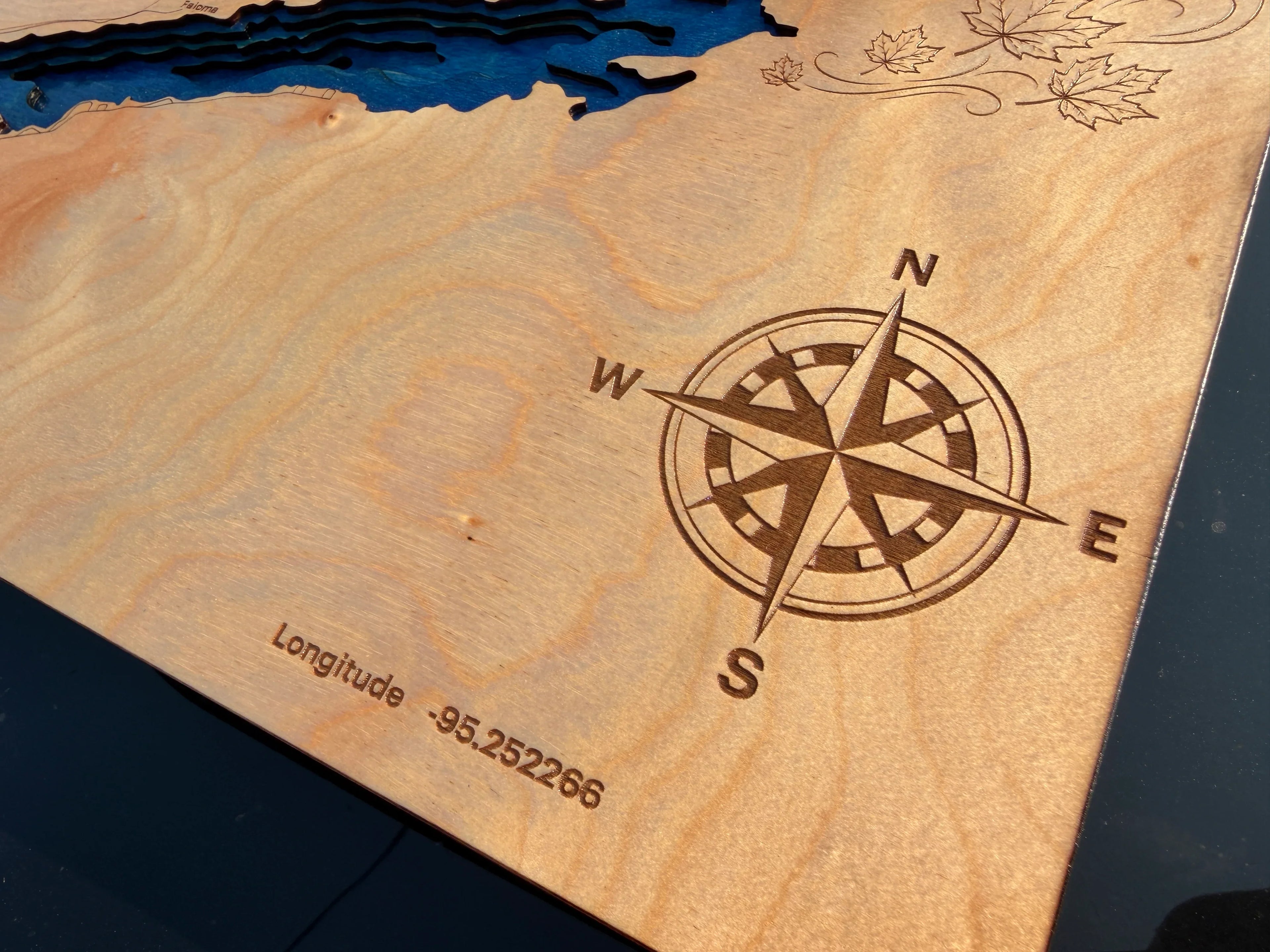 Laser-cut wooden lake map with engraved compass rose and coordinates, featuring layered depth design and maple leaf details.