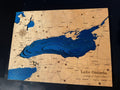A rectangular wooden map plaque featuring Lake Ontario in deep blue with engraved land details and labels, including 'Lake Ontario Canada & United States' and coordinates, photographed on a dark background.