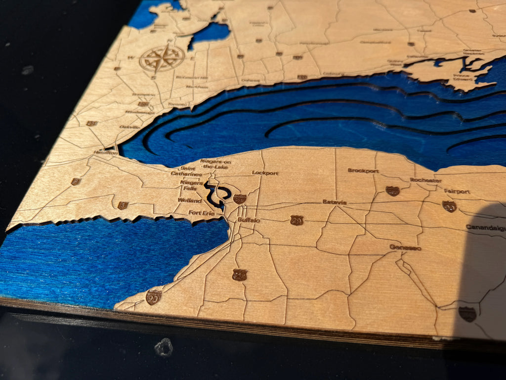 A close-up of a wooden map wall art piece showing the Great Lakes and surrounding states, with layered wood and deep blue recessed water areas.