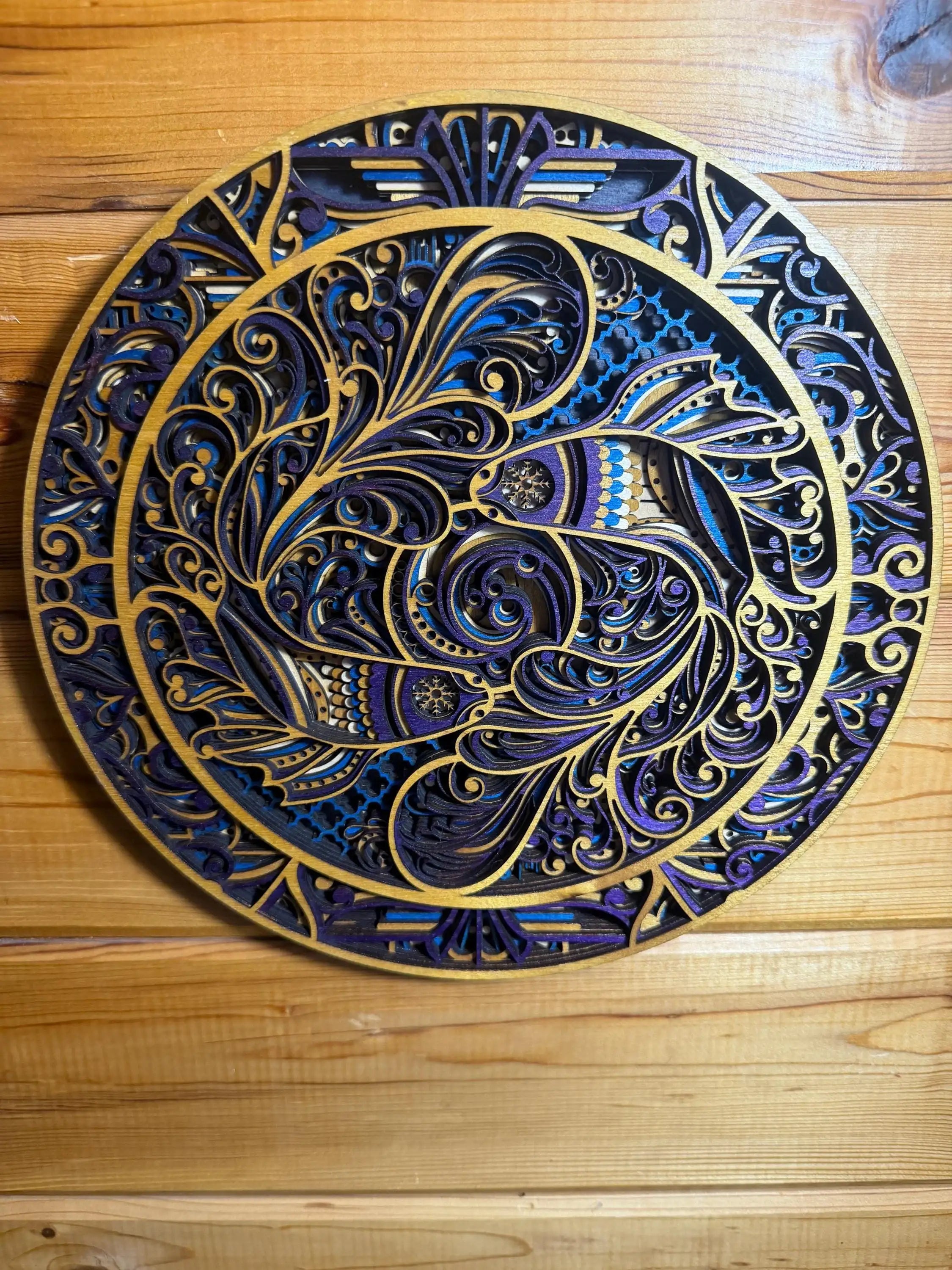 Layered wood mandala wall art with intricate blue, purple, and gold laser-cut swirls on rustic wood background