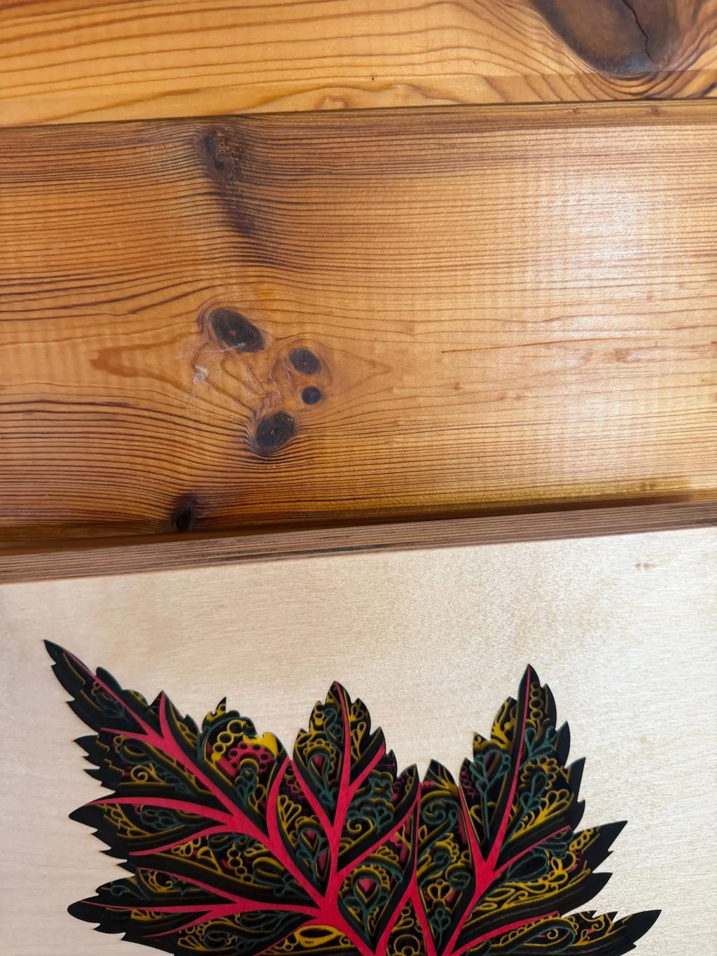 Layered wood art with intricate leaf design, vibrant red and yellow details on natural wood background