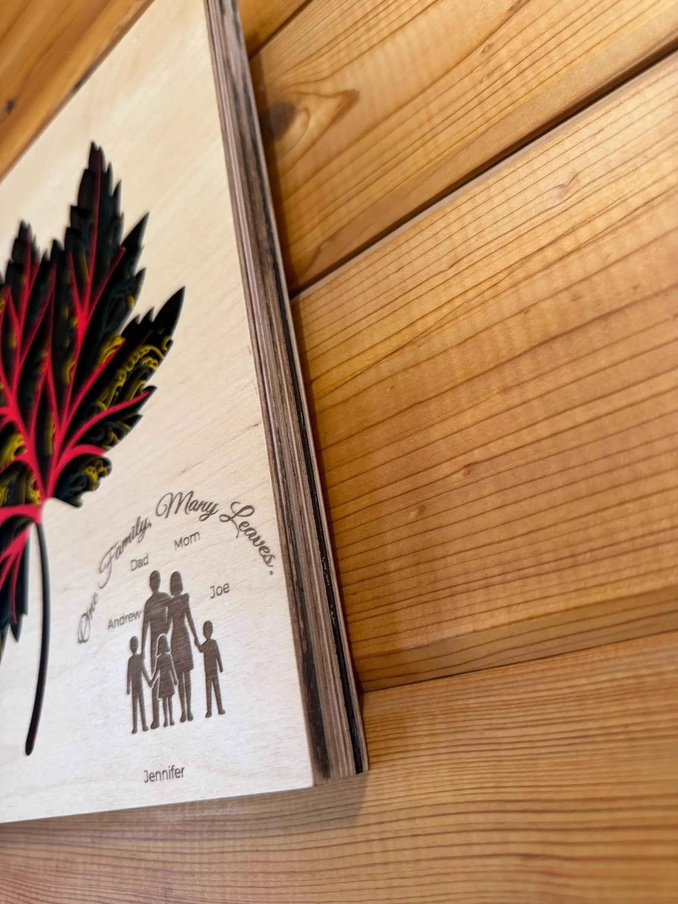 Layered wood family art with colorful leaf design, personalized names, and 'One Family, Many Leaves' quote on rustic wood wall