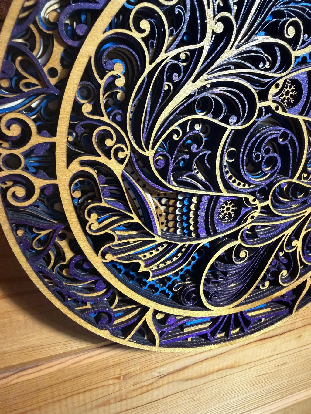 Intricate layered wood mandala with blue, purple, and gold swirls, laser-cut for unique decor.