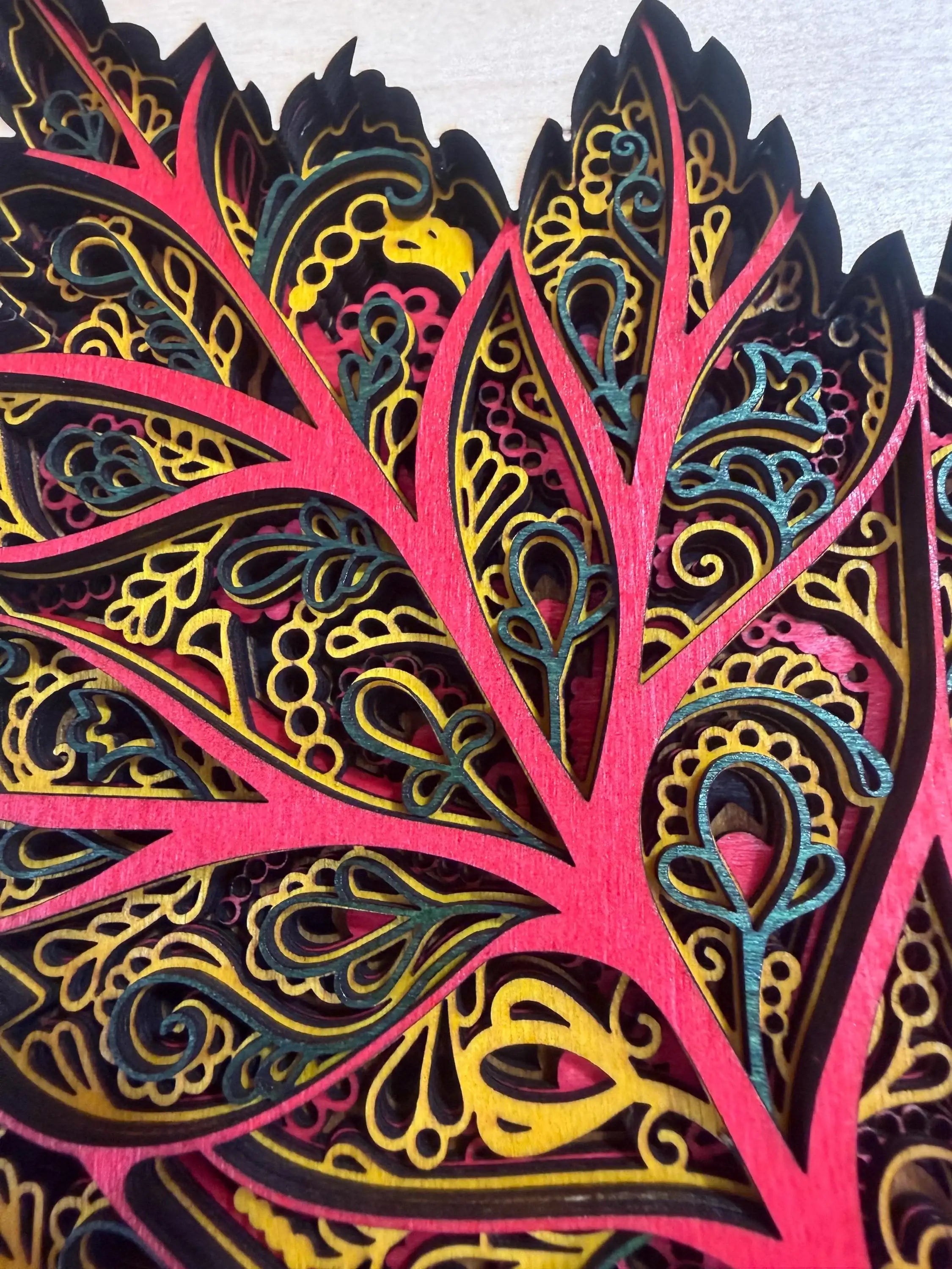 Vibrant layered wood mandala with intricate laser-cut patterns in pink, gold, and teal