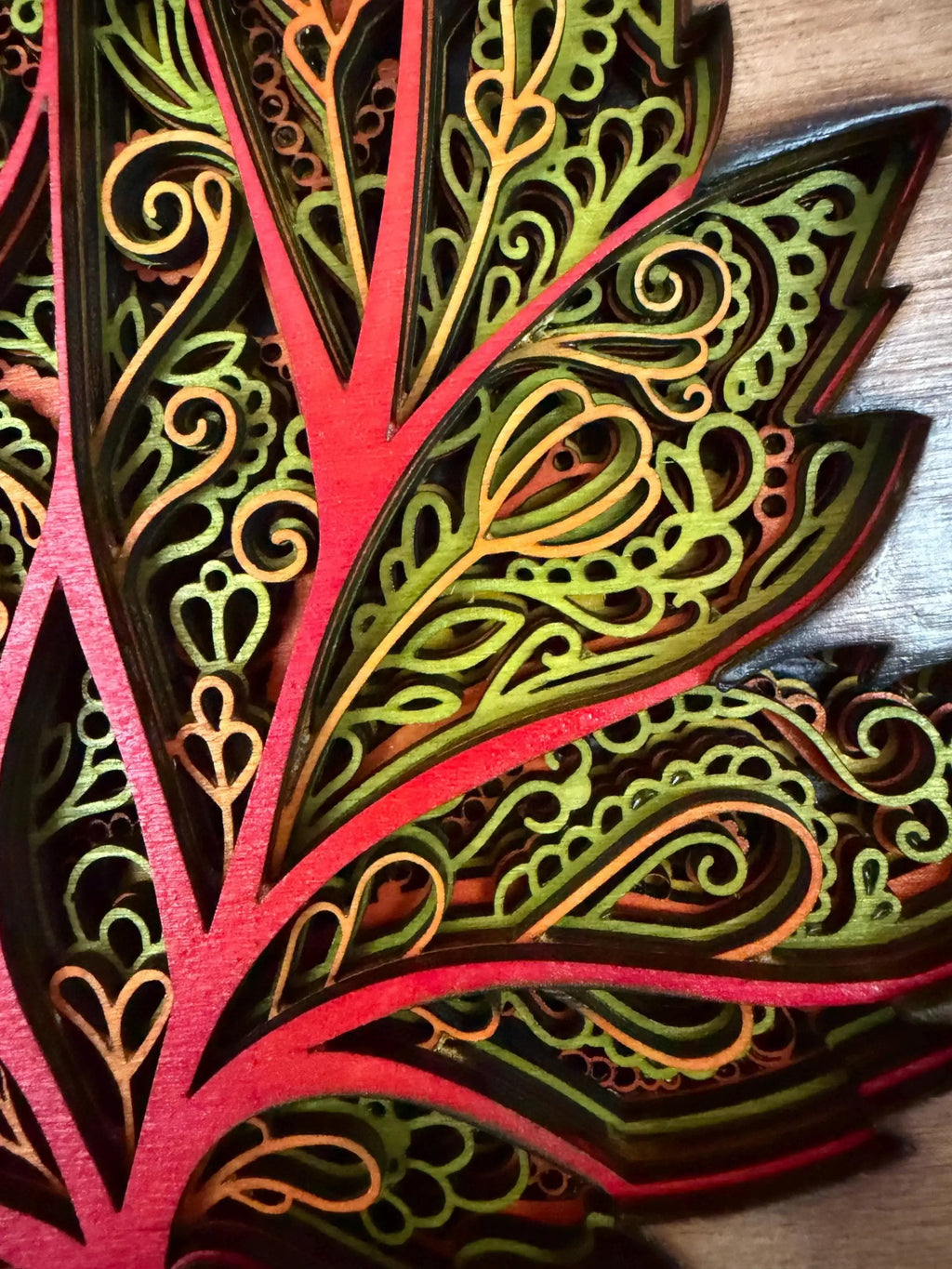 Intricate layered wood art with vibrant red, green, and gold laser-cut patterns, showcasing detailed mandala-style design.