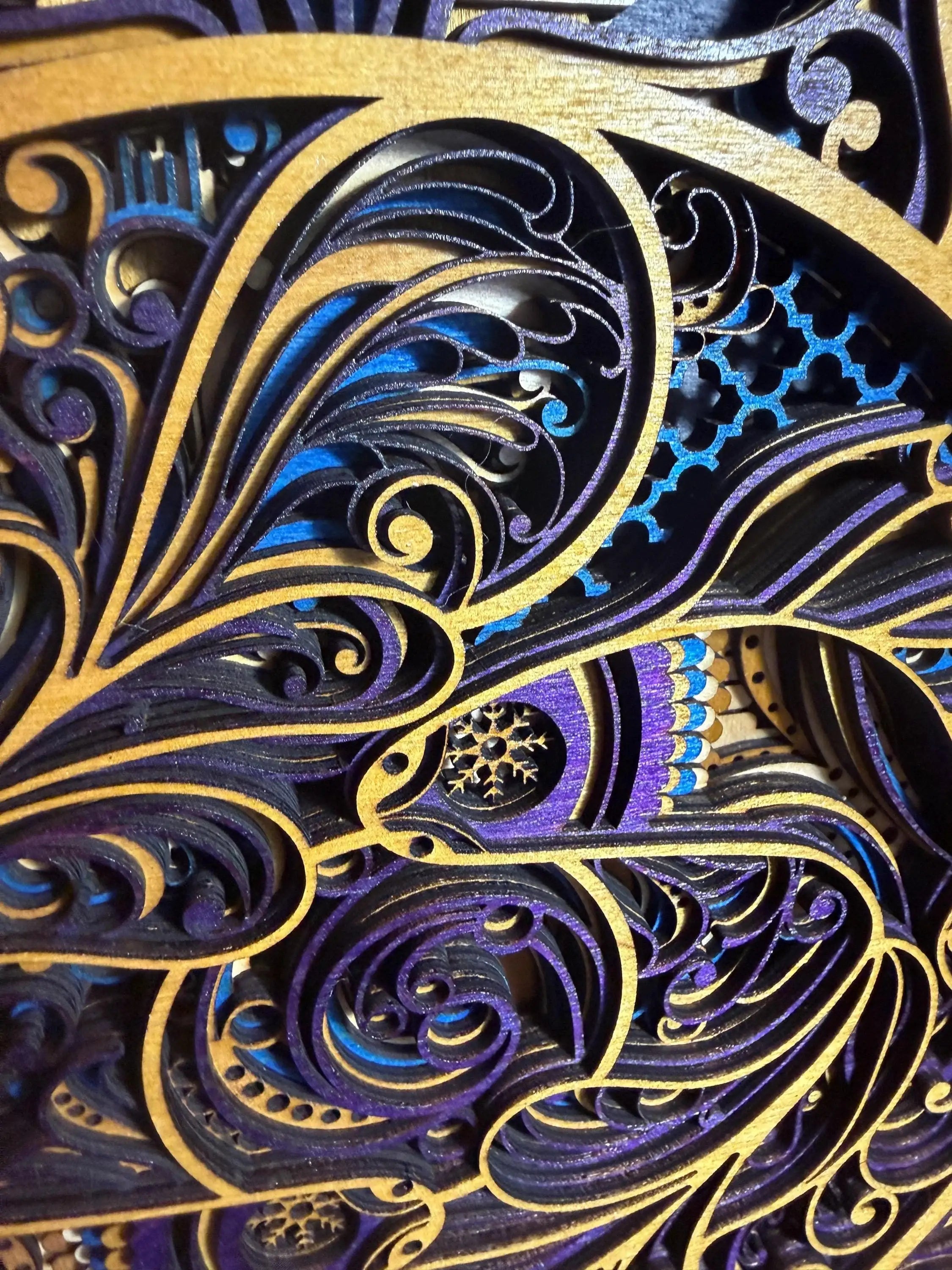 Intricate layered wood art with swirling purple, blue, and gold patterns, featuring laser-cut details and a snowflake motif.